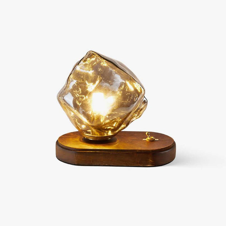 Szklana designerska lampa stołowa w kształcie bryły lodu z bursztynowym odcieniem na stole