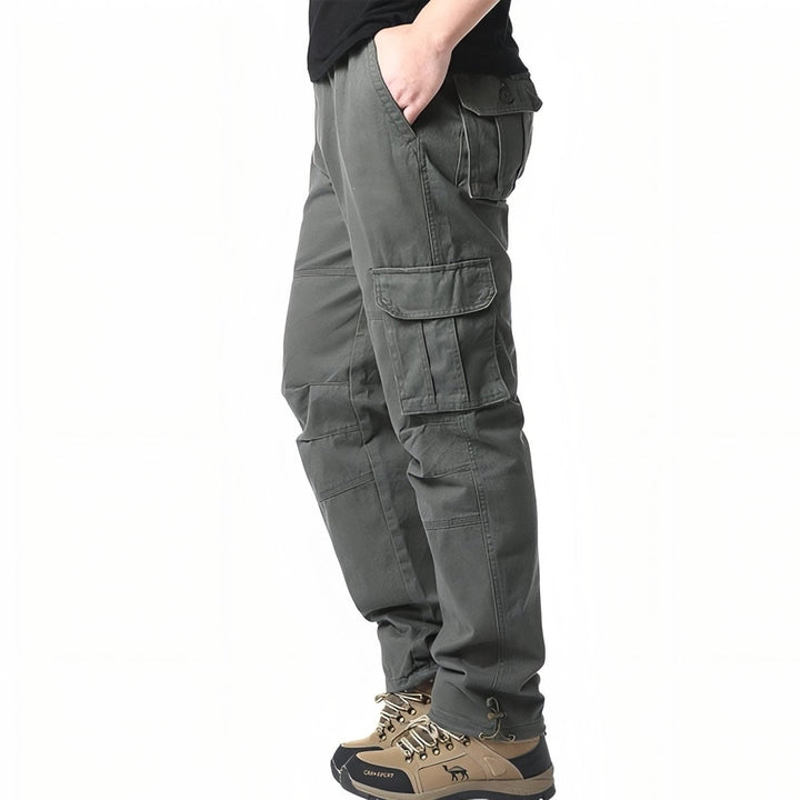 Szczegół męskich spodni trekkingowych pokazujący kieszeń cargo i elastyczną talię, w kolorze oliwkowym.