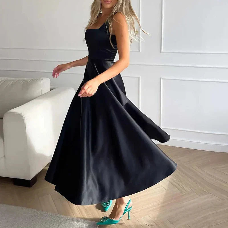 Modelka prezentująca satynową sukienkę midi A-line w eleganckim stylu, z kwadratowym dekoltem i ramiączkami spaghetti.